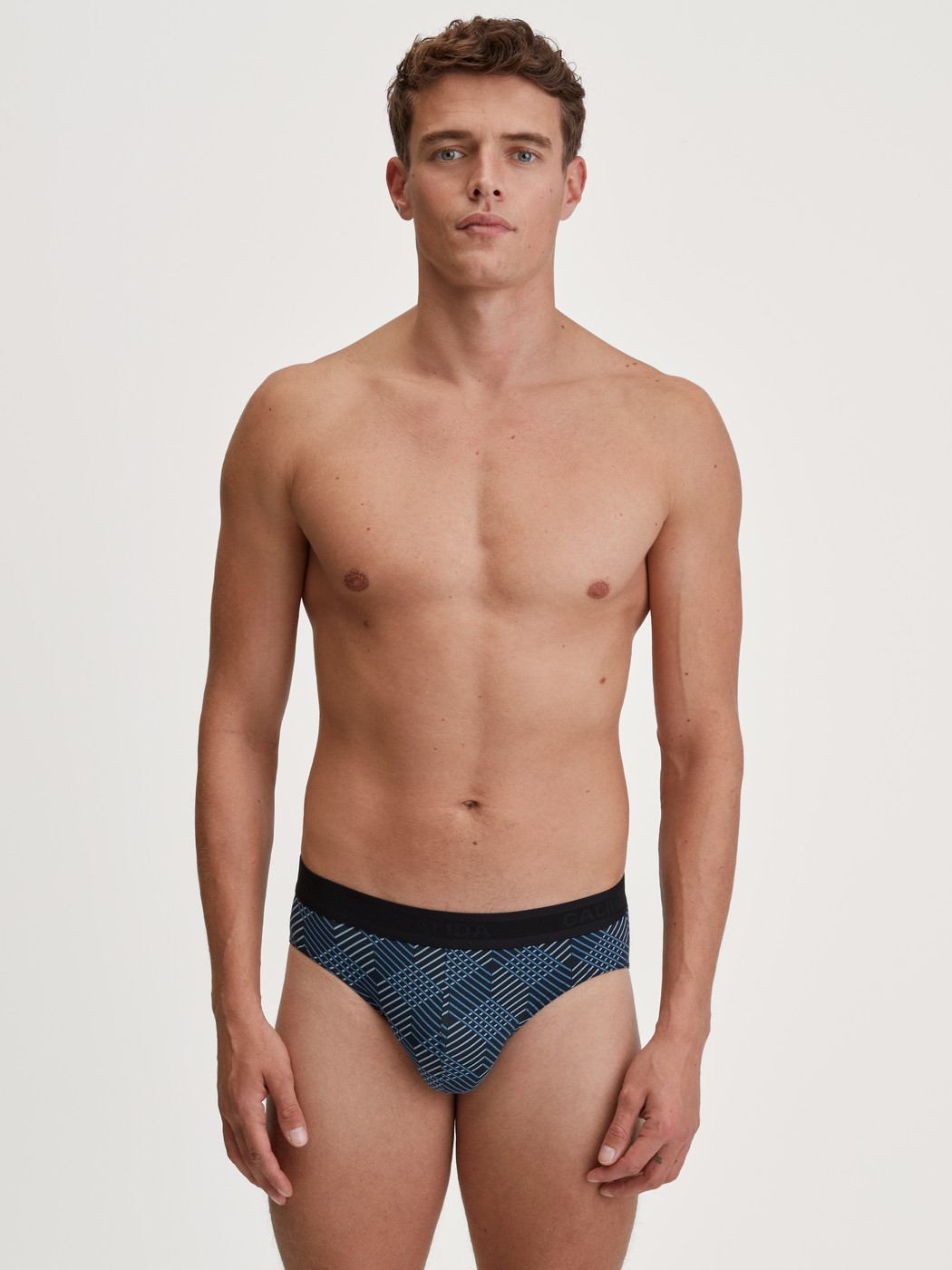 Herren-Model trägt Slip mit Softgummibund aus Baumwolle in Schwarz, Gemustert aus Serie Grafic Cotton von CALIDA, Outfit