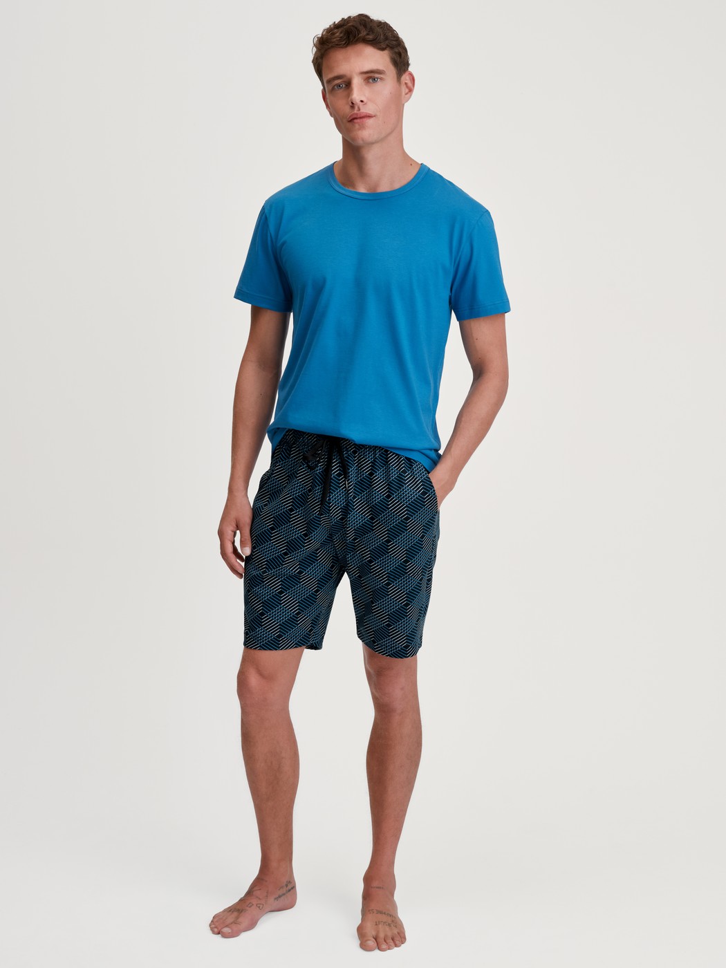 Herren-Model trägt Bermudas aus 100% Baumwolle in Schwarz, Gemustert aus Serie RMX Sleep Leisure von CALIDA, Outfit