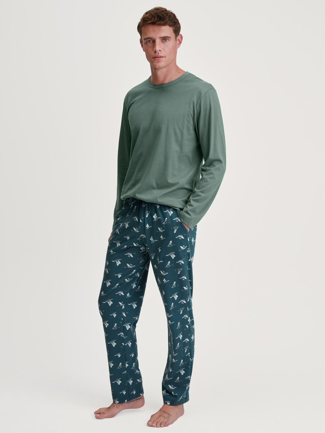 Herren-Model trägt Pyjamahose mit Seitentaschen aus 100% Baumwolle in Grün, Gemustert aus Serie RMX Sleep Weekend von CALIDA, Outfit