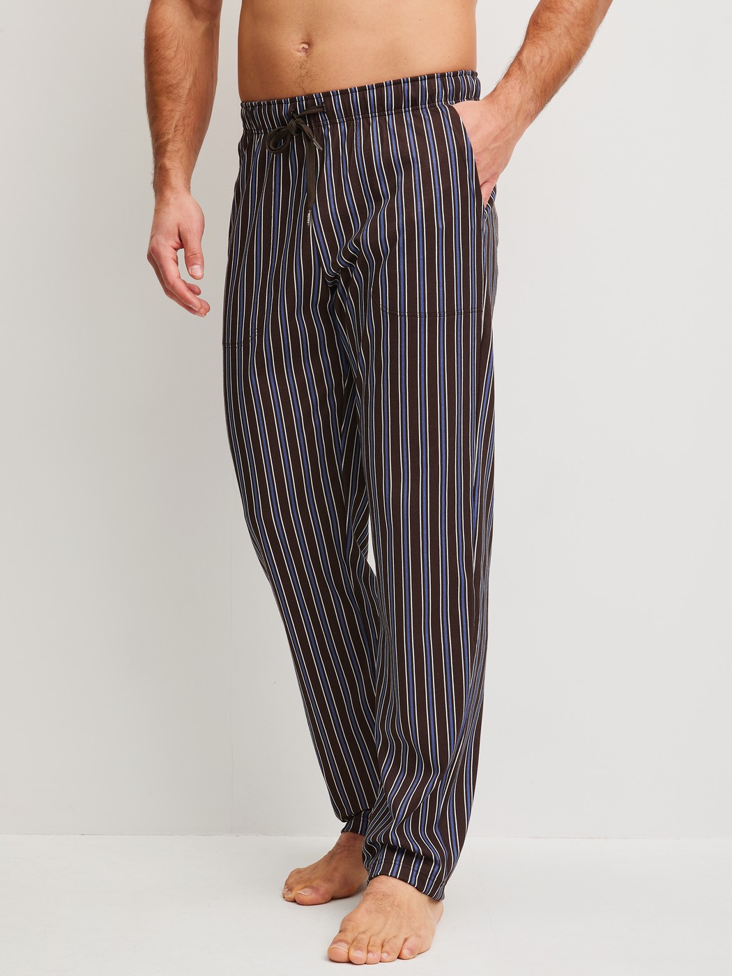 Men model is wearing Pyjama Bottoms with Side Pockets made of 100% Cotton in Brown, Striped from the RMX Sleep Weekend series by CALIDA, Front view