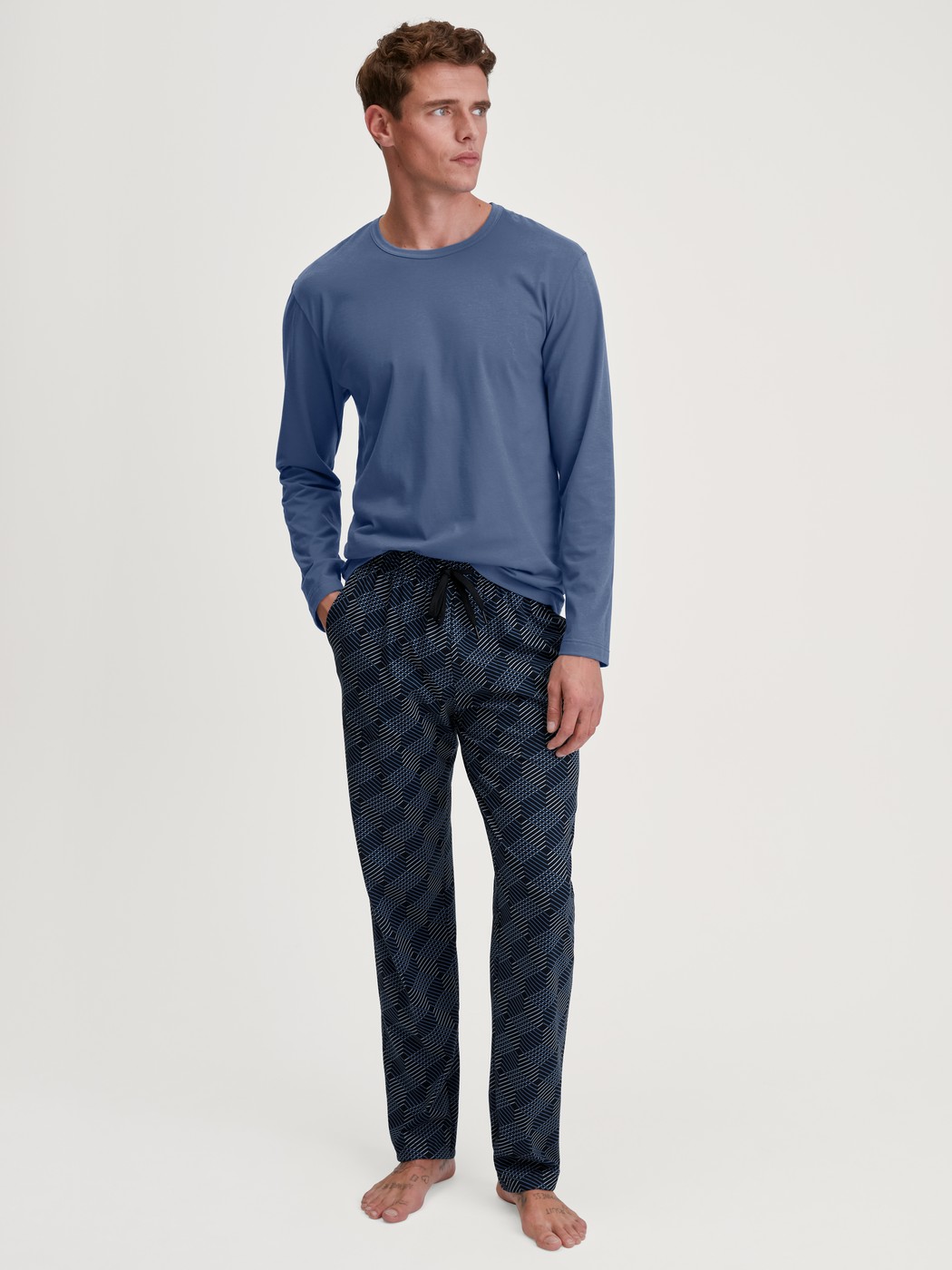 Herren-Model trägt Pyjamahose mit Seitentaschen aus 100% Baumwolle in Schwarz, Gemustert aus Serie RMX Sleep Leisure von CALIDA, Outfit