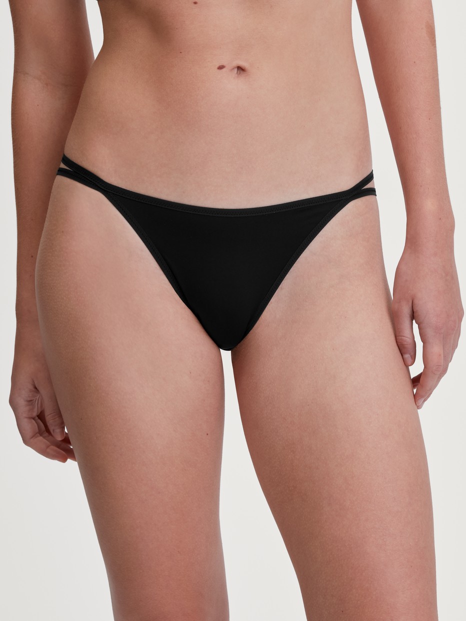 Damen-Model trägt Tanga-Slip, low cut aus Polyamid in Schwarz, Einfarbig aus Serie Sleek Skin von CALIDA, Vorderansicht
