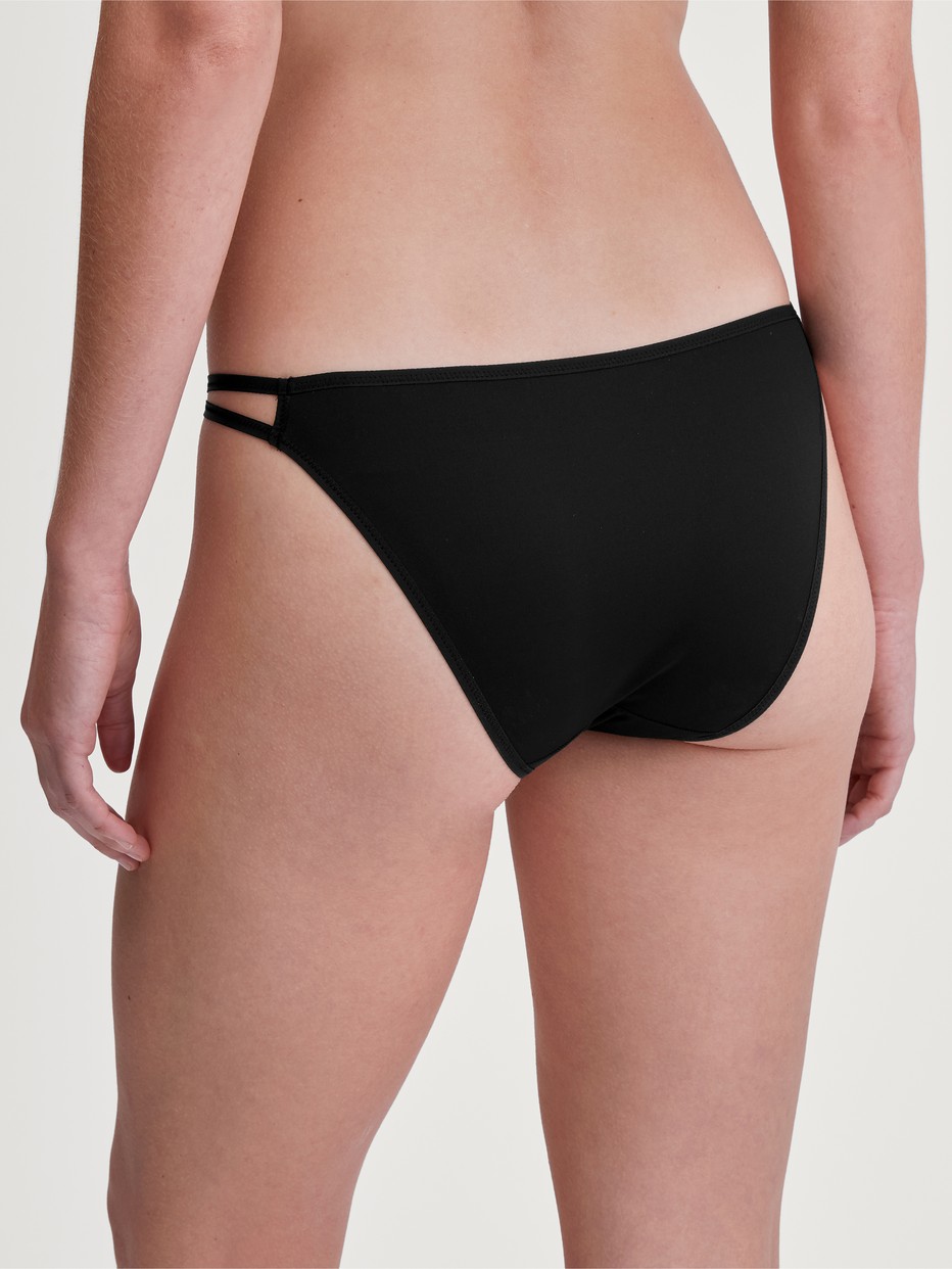 Damen-Model trägt Tanga-Slip, low cut aus Polyamid in Schwarz, Einfarbig aus Serie Sleek Skin von CALIDA, Vorderansicht