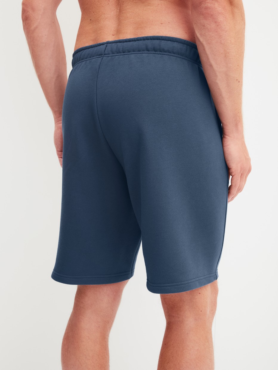 Men model is wearing Bermudas with side pockets made of Cotton in Blue, Unicoloured from the RMX Lounge Journey series by CALIDA, Back view