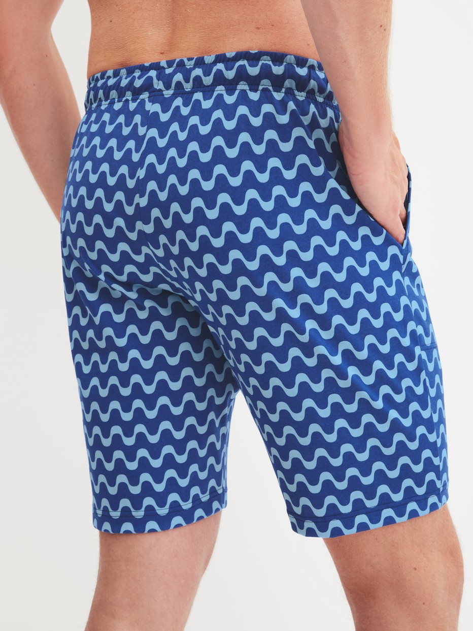 Men model is wearing Bermudas made of 100% Cotton in Blue, Patterned from the RMX Sleep Time off series by CALIDA, Back view