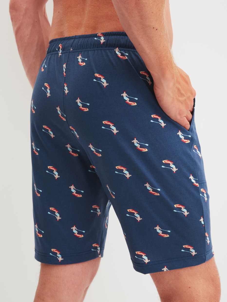 Herren-Model trägt Bermudas aus 100% Baumwolle in Blau, Gemustert aus Serie RMX Sleep Holiday von CALIDA, Rückansicht