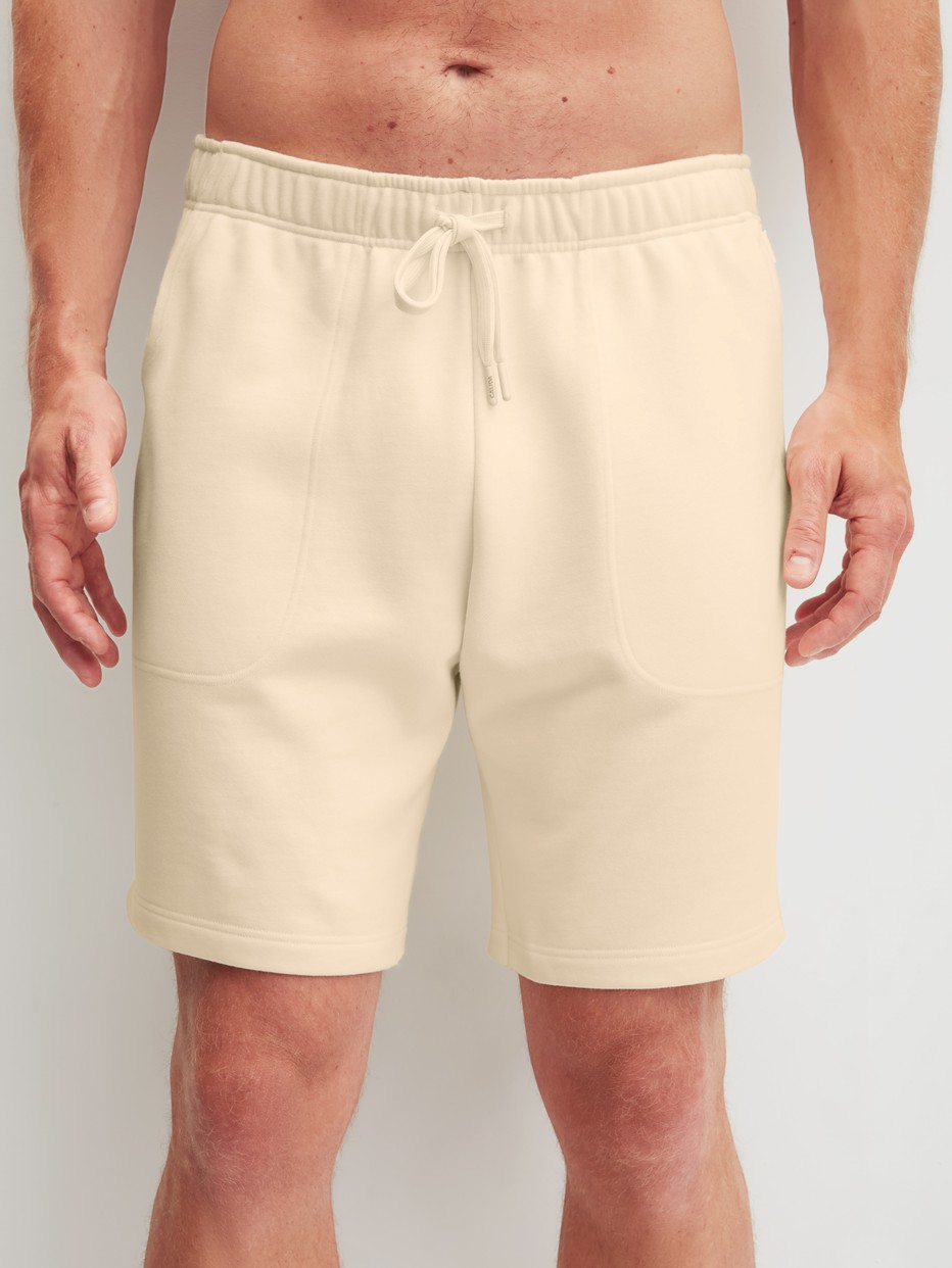 Herren-Model trägt Bermudas mit Seitentaschen aus Baumwolle in Beige, Einfarbig aus Serie RMX Lounge Lecce von CALIDA, Vorderansicht