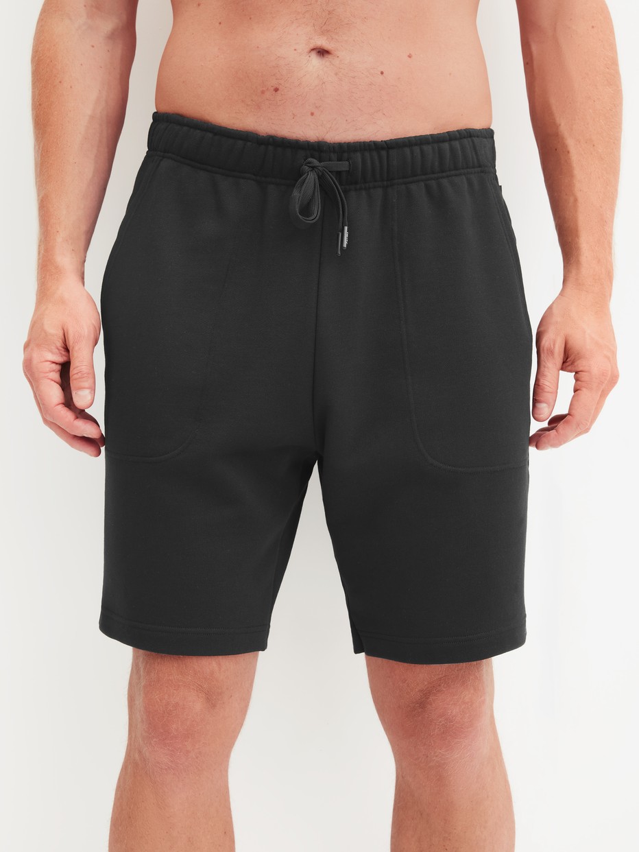 Herren-Model trägt Bermudas mit Seitentaschen aus Baumwolle in Schwarz, Einfarbig aus Serie RMX Lounge Lecce von CALIDA, Vorderansicht