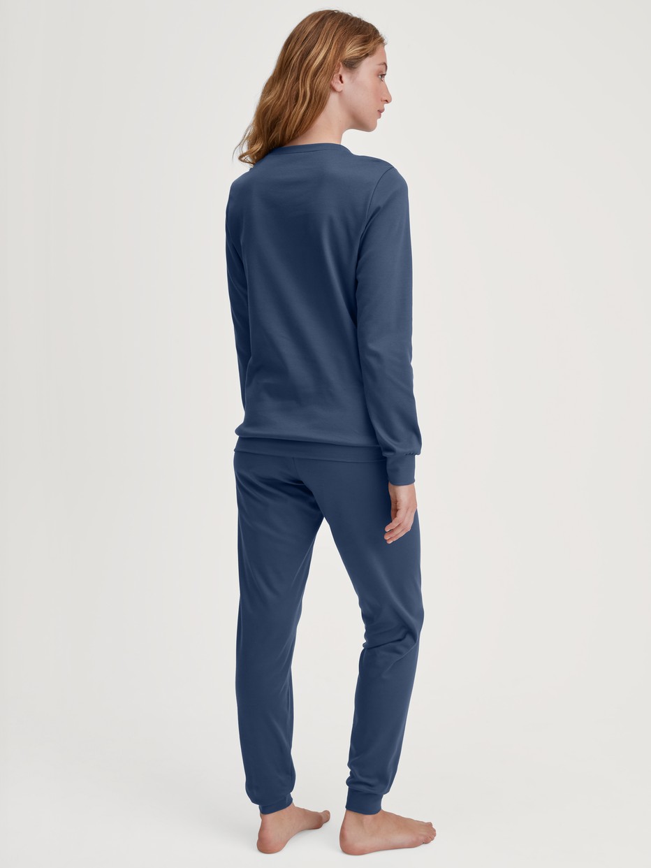 Damen-Model trägt Bündchen-Pyjama aus 100% Baumwolle in Blau, Motiv aus Serie Ski Resort von CALIDA, Rückansicht