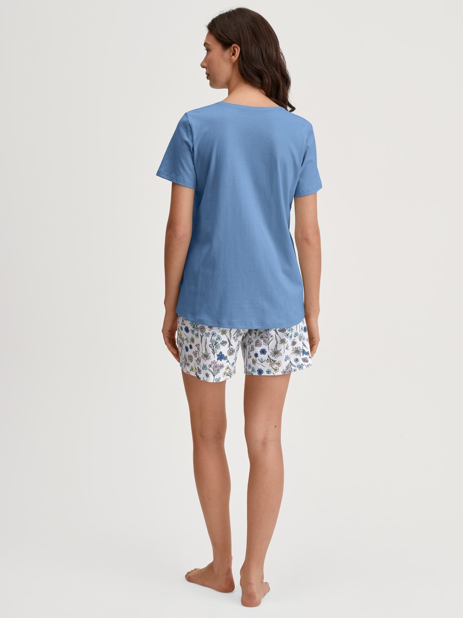 Damen-Model trägt Kurz-Pyjama aus 100% Baumwolle in Blau, Floral aus Serie Flower Nights von CALIDA, Rückansicht